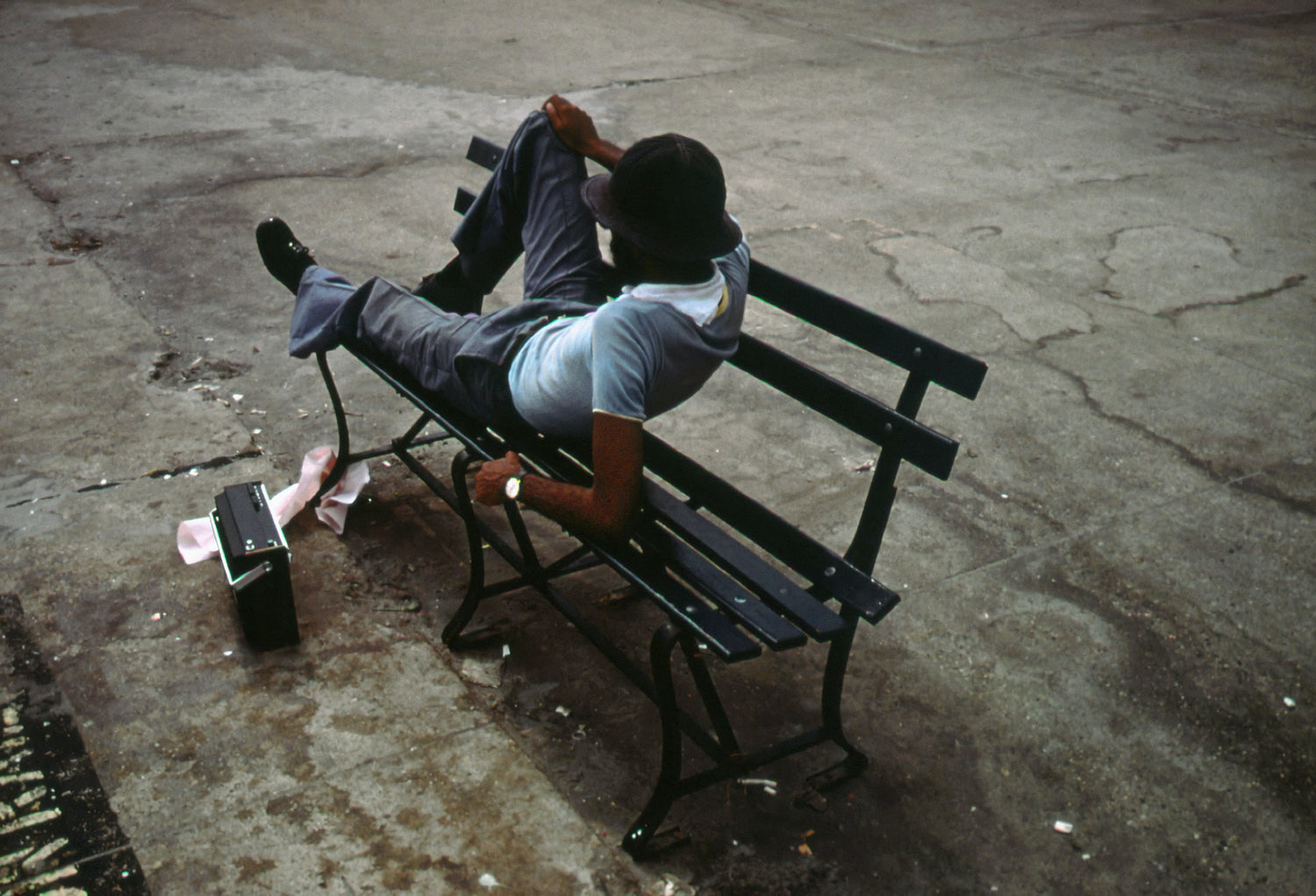 A man lounging on a park bench with a transistor radio.